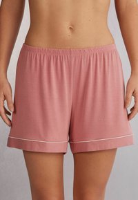 Rosa bomullsshorts med en mjuk textur, med ett elastiskt midjeband och vita detaljer vid fållen. Avslappnad passform och knä-lång längd.