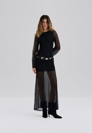 Svart kjole med lange gjennomsiktige stripete ermer, en tettsittende bodice og en flytende skjørt med et solid underlag. Akkompagnert med et svart belte.