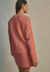 Kootud tweed jakk ja seelik komplekt roosas, mitmevärviliste aktsentidega. Omab pikki varrukaid ja klassikalist siluetti, tekstureeritud pinnakatte detail.