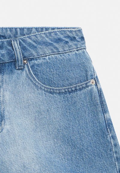 Blugi din denim albastru deschis, prim-plan, care arată talia, bucla de curea, buzunarul frontal și nituri metalice pe un fundal alb.