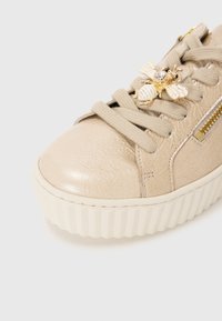 Baskets en cuir beige avec surface texturée, bout arrondi et semelle en caoutchouc. Présentent un design à lacets et un accent décoratif en forme d'abeille avec strass.