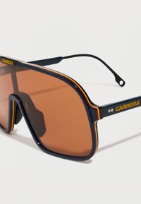 Gafas de sol con lentes marrones oscuros, montura azul con rayas amarillas y rojas, y logo de Carrera en las patillas.