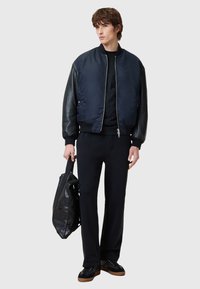 Navy bomber jacket with black leather sleeves, zip closure, paired with black trousers and a black leather bag, featuring textured accents.