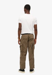 Cargo pants in olijfgroen stof, met zijzakken, een relaxte pasvorm en een iets toelopende pijp. Gecombineerd met een wit t-shirt.