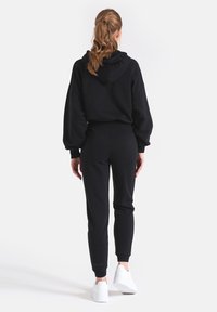 Czarna bluza z kapturem i oversize'owymi rękawami oraz ściągaczem, w zestawie z dopasowanymi, zwężanymi spodniami dresowymi. Bluza ma elastyczną talię i ściągacze przy kostkach. Do tego białe sneakersy.