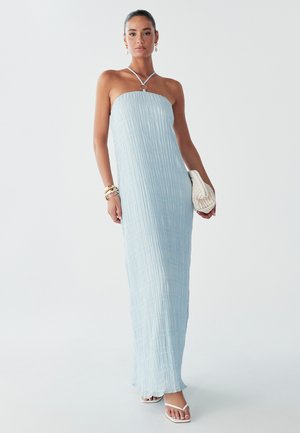 Das Model posiert in einem hellblauen, schulterfreien Maxikleid mit strukturiertem Design. Es hält eine kleine weiße Tasche und trägt goldene Accessoires sowie Sandalen.