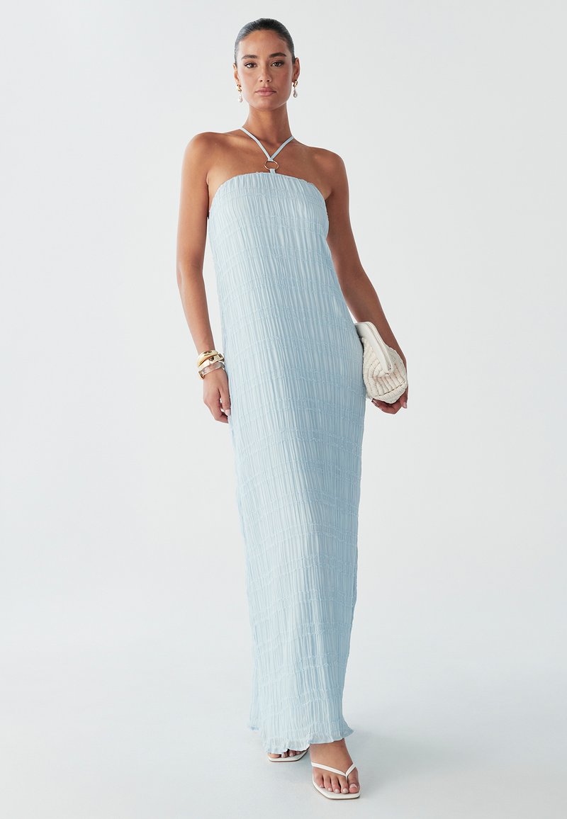 Svetlo modra, obleka brez naramnic z teksturiranim, nabranskim vzorcem. Ima obročkasto detajl pri izrezu in sega do maxi dolžine. Oblečena z belimi sandali.