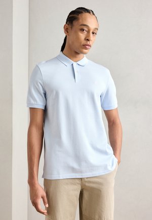 Polo en coton bleu clair avec un col classique, des manches courtes et un petit logo sur la poitrine, associé à un short beige.