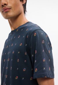 Μπλέ μπλουζάκι κοντ ό μανίκι με πολύχρωμο σχέδιο μικρών εντόμων σε όλη την επιφάνεια. Μαλακό βαμβακερό ύφασμα με σχέδιο κολοβού λαιμού.