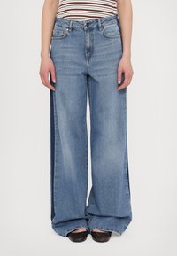 Light blue, high-waisted wide-leg jeans with a relaxed fit, featuring front pockets and a distinctive side panel design.