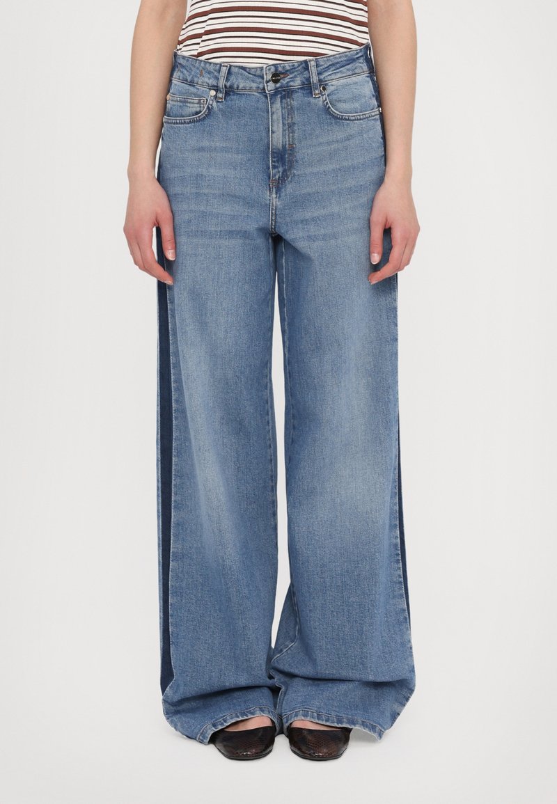 Light blue, high-waisted wide-leg jeans with a relaxed fit, featuring front pockets and a distinctive side panel design.