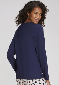 Navy blue long-sleeve top made of soft material, featuring a round neckline and relaxed fit, worn with patterned light pants.