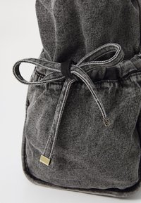 Schwarze und graue strukturierte Stoff-Zugtasche mit einem glänzenden goldenen Akzent am Verschluss. Verfügt über einen gerafften oberen Bereich und eine weiche Körperform.