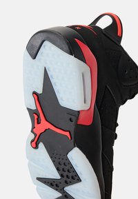 Črni in rdeči športni copat, ki prikazuje podplat z rdečo silhueto Jumpman in prozornimi detajli tekalne površine.