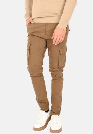 Pantaloni cargo beige dalla vestibilità slim, con molteplici tasche laterali e una superficie liscia. Abbinati a sneakers bianche e una maglietta beige.
