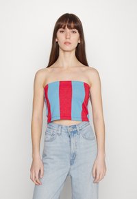 Top cropped sem alças, às riscas vermelhas e azuis, feito de um tecido elástico, usado com jeans de cintura alta de tom azul claro.