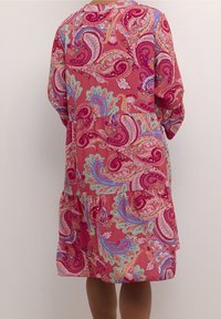 Różowa sukienka w wzór paisley o luźnym kroju, z długimi rękawami, warstwowym designem i miękką teksturą. Posiada żywe niebieskie i zielone akcenty.