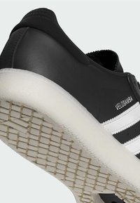 Czarne skórzane sneakersy z białymi paskami, teksturowana gumowa podeszwa i gładka cholewka. Posiadają wzmocnioną piętę oraz zaokrąglony nos.
