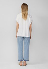 Witte, losse T-shirt met opgerolde mouwen, gecombineerd met lichtblauwe, wijdvallende jeans met een contrasterende zoom. Eenvoudig, casual ontwerp.