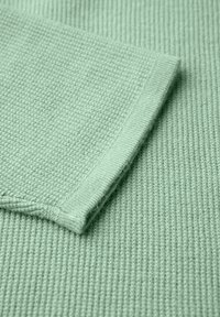 Tessuto verde chiaro con una texture rigata, caratterizzato da un bordo piegato. La superficie è morbida con una tessitura uniforme.
