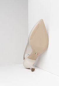 Scarpa con tacco alta beige in pelle liscia con punta affusolata, caratterizzata da un piccolo design a intaglio e una suola lucida di colore crema.