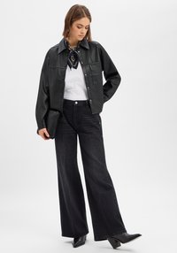 Zwarte leren jas met een kraag, knoopsluiting en een voorvak, gecombineerd met wijde donkere jeans en zwarte laarzen met hak.