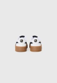Baskets blanches avec une rayure noire, présentant une semelle plateforme texturée marron et un accent logo rond sur le talon.