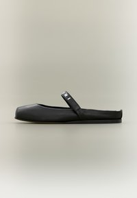 Chaussure plate noire à bout carré, en matériau synthétique lisse, avec une bride latérale et une semelle basse. Design minimaliste.