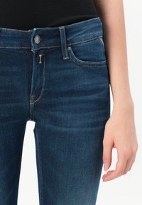 Mørkeblå denimjeans med en tett passform, standard fem-lommers stil og kontrasterende gyllen søm langs sømmene.
