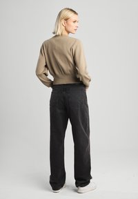 Beige cropped sweater with long sleeves, textured knit fabric. Paired with high-waisted black denim jeans. Model facing backward.