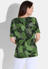 Korte mouw top met een groene bladerenpatroon op een zwarte achtergrond. Zachte stof en een losse pasvorm met een ronde hals.