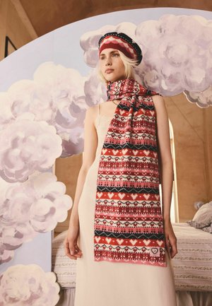 Strickschal mit roten, rosa, schwarzen und weißen geometrischen Mustern, Herzmotiven und einem Stoffetikett, um den Hals eines Modells drapiert.