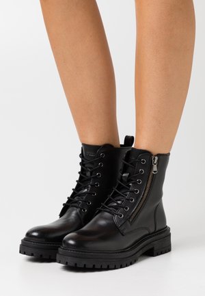 Svarta läderkängor med snörning framtill, sidodragkedja och robust sulprofil. Har en slät yta och förstärkta sömmen.