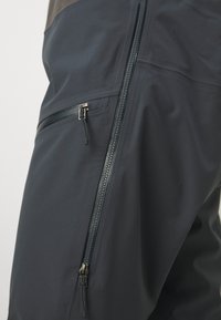 Tummansininen tekninen housut, joissa on vetoketjut sivuilla, sileä pinta ja tiukka istuvuus, joka parantaa liikkuvuutta.