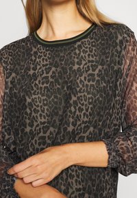 Hienoa puseroa, jossa on leopardi-printti tummanvihreänä ja ruskeana. Ominaisuuksiin kuuluu ribbireunus ja kerrostetut hihansuut. Kevyt, virtaava rakenne.
