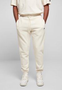 Pantalones de chándal color crema hechos de una tela suave, con una cintura ajustable con cordón, bolsillos laterales y un pequeño logotipo bordado en el muslo izquierdo.