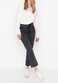 Chemise blanche à rayures verticales avec manches longues, associée à un jean noir délavé à coupe droite et des baskets blanches. Tenue simple et décontractée.