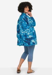 Maglietta blu tie-dye con un fit ampio, maniche lunghe e colletto. Abbinata a jeans in denim cropped e sandali leggeri.