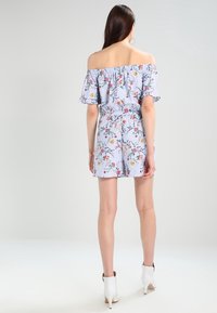 Modrý a bílý pruhovaný overal s odhalenými rameny, květinovým potiskem, volánkovými rukávy, stahovacími šňůrkami v pase a kraťasy. Nohy má obuté do bílých lodiček.