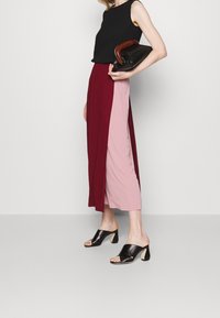 Haut sans manches noir texturé associé à une jupe bicolore en bourgogne et rose. Mules noires à talons avec un design à bout ouvert.