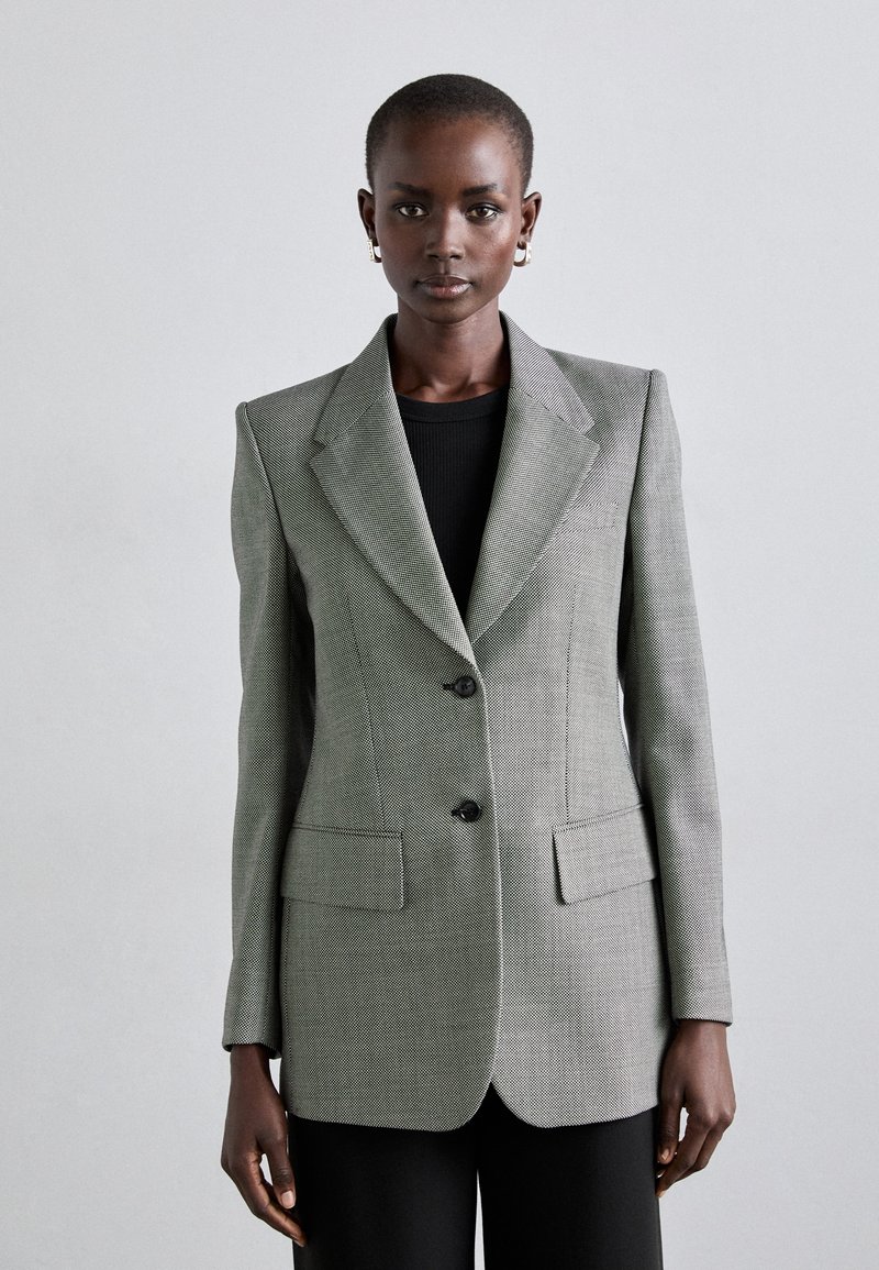 Harmaa teksturoitu bleiseri, jossa on istuva malli, viistot kaulukset, kaksi etutaskua ja tummat napit. Päällä musta paita.