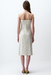 Blumenkleid midi mit dünnen Trägern. Weißer Stoff mit kleinen blauen und gelben Blumen. Glatter Stoff, endet knapp unter dem Knie.