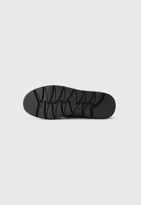 Suela de zapato negra con patrones de tracción profundos y angulares y la marca "ecco" en el centro, presentada en plano sobre un fondo blanco.