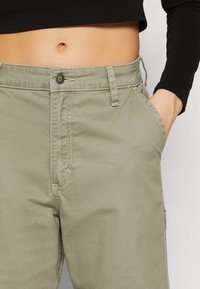 Khaki zelené cargo kalhoty s úzkým střihem, s knoflíkovým zapínáním, bočními kapsami a viditelným švem podél švů.