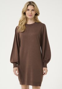 Abito di maglia marrone con collo rotondo, maniche lunghe a palloncino e polsini a coste. Il tessuto ha una consistenza liscia e una vestibilità ampia.