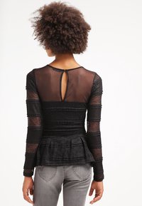 T-shirt noir à manches longues avec un ourlet peplum, présentant des accents rayés transparents et une fermeture en forme de trou de serrure au dos. Tissu texturé avec des éléments de design superposés.