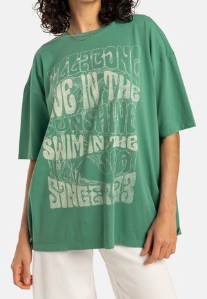 T-shirt vert surdimensionné en coton, avec un texte blanc audacieux et un design abstrait. Manches courtes et coupe ample avec des fentes sur les côtés.