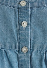 Primo piano di un tessuto denim blu con tre bottoni bianchi e dettagli di cucitura lungo la patta dei bottoni.