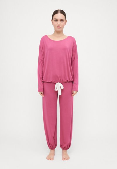 Ensemble de détente rose comprenant un haut à manches longues ample et un pantalon à taille élastique. Le pantalon est doté d'un cordon blanc. Texture douce et lisse.