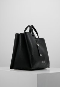 Czarna skórzana torba na ramię o teksturowanym wykończeniu, z dwiema górnymi ramiami i subtelnymi metalowymi akcentami, charakteryzująca się przestronnym, usztywnionym kształtem.